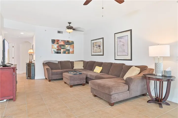 Spacious living area featuring neutral tile flooring, white walls, and a ceiling fan