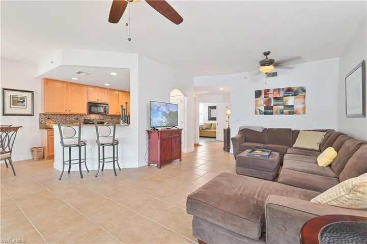 Open-concept living area featuring tile flooring, a kitchen pass-through with breakfast bar, recessed lighting, and ceiling fans