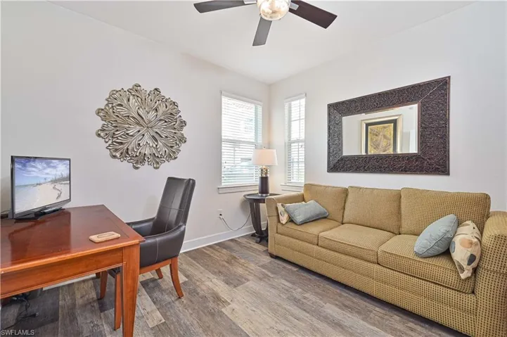 Spacious room featuring wood-finish flooring, multiple windows with blinds, a ceiling fan, and white walls