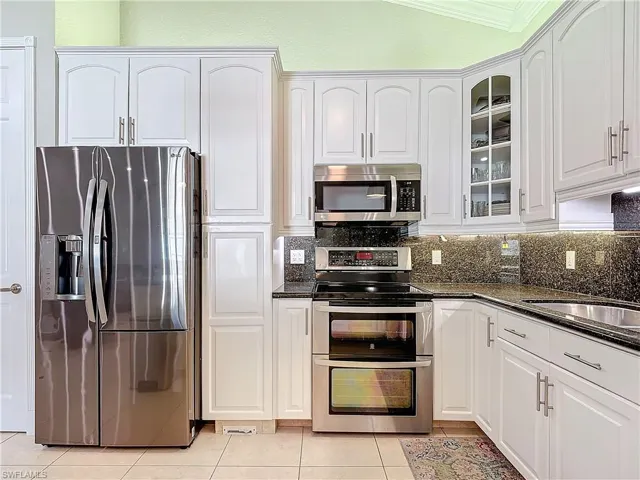 Kitchen with stainless steel appliances, dark stone countertops, white cabinetry, light tile patterned floors, and glass insert cabinets