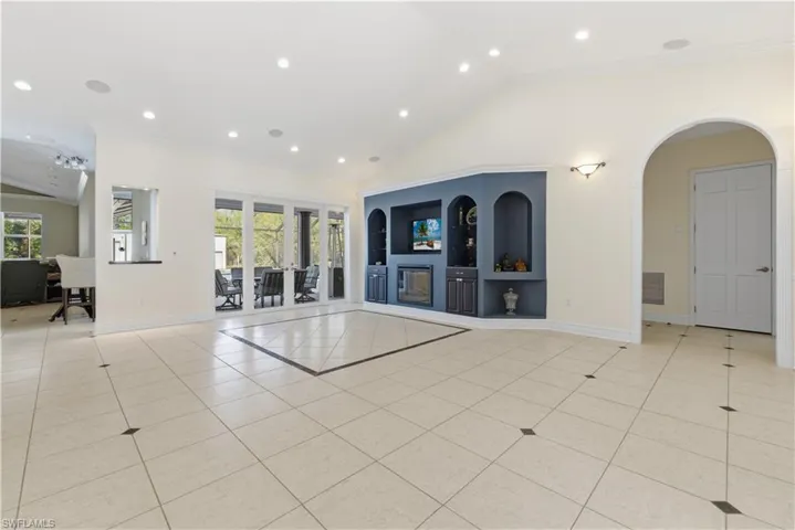 Unfurnished living room featuring lofted ceiling, built in shelves, light tile patterned floors, recessed lighting, and ornamental molding