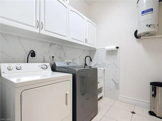 Washroom featuring cabinet space, washing machine and clothes dryer, and light tile patterned floors