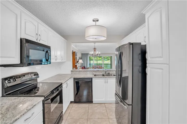 Kitchen with black appliances, a notable chandelier, light tile floors, hanging light fixtures, and sink