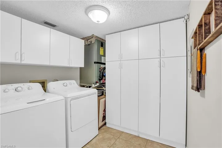 Laundry area with cabinets, water heater, washer hookup, washing machine and dryer, and a textured ceiling