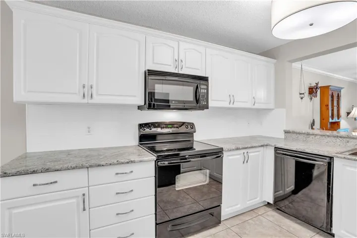 Kitchen featuring crown molding, light tile flooring, black appliances,  and white cabinetry
