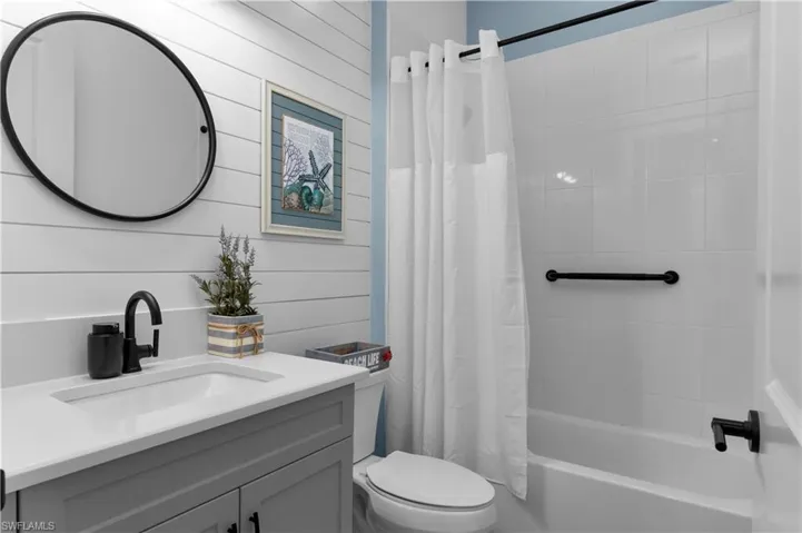 Full bathroom with vanity, shower / tub combo with curtain, and wooden walls
