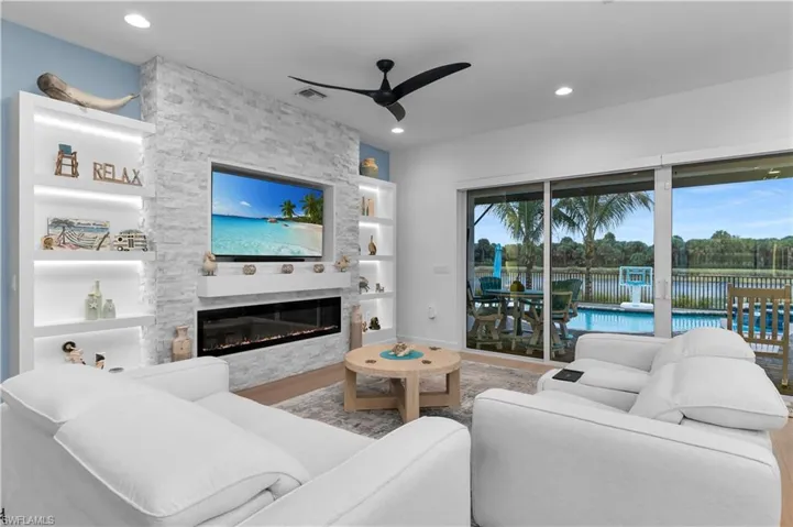 Living room featuring built in features, a stone fireplace, ceiling fan, recessed lighting, and wood finished floors