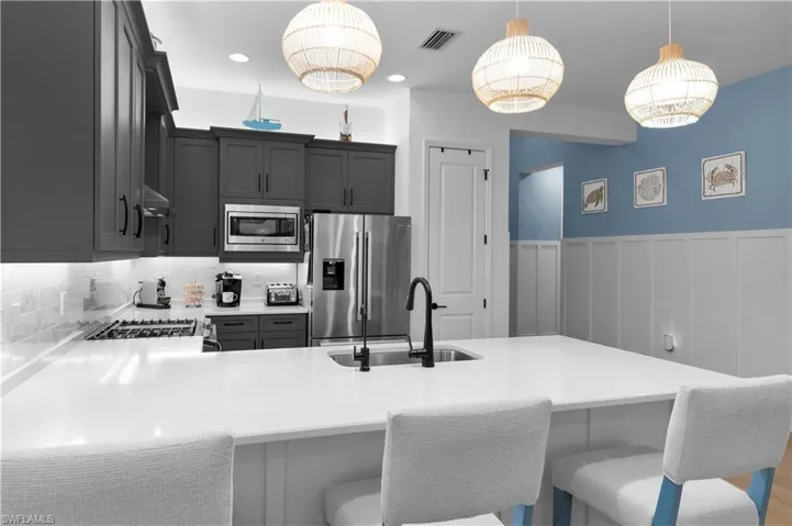 Kitchen featuring appliances with stainless steel finishes, a peninsula, hanging light fixtures, a breakfast bar, and wainscoting