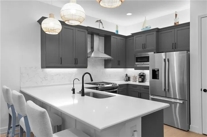 Kitchen featuring appliances with stainless steel finishes, wall chimney exhaust hood, backsplash, a peninsula, and hanging light fixtures