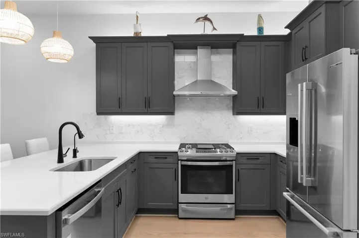 Kitchen with stainless steel appliances, a peninsula, wall chimney exhaust hood, light stone countertops, and gray cabinets