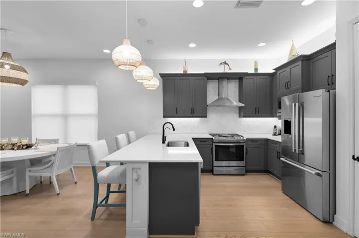 Kitchen with a kitchen bar, a peninsula, stainless steel appliances, tasteful backsplash, and wall chimney exhaust hood