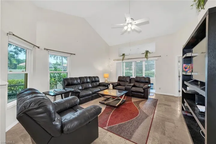 Vaulted ceiling living area featuring tile flooring, a ceiling fan, and large windows