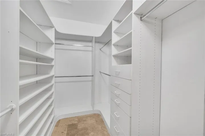 Custom walk-in closet featuring white built-in shelving, multiple hanging rods, and integrated drawers with white pulls