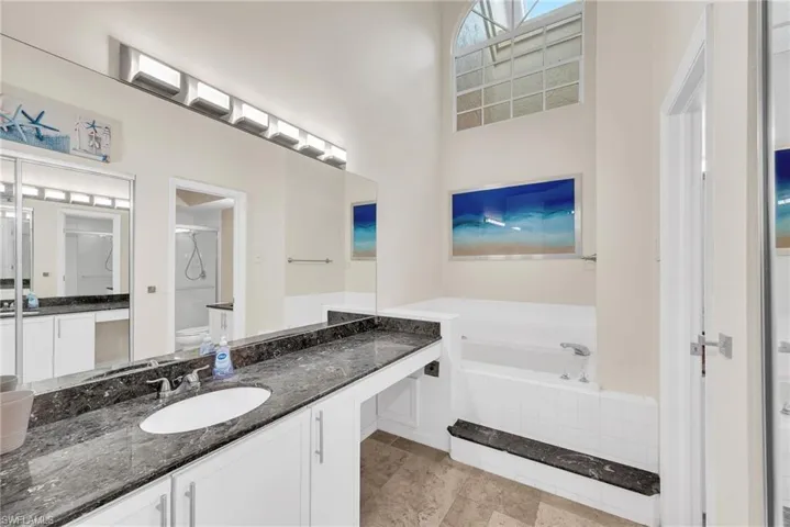 Spacious bathroom featuring an arched transom window, a deep soaking tub, and a dual vanity with a dark stone countertop