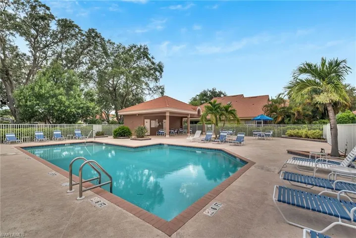 Resort-style pool area featuring a perimeter fence, a covered cabana, and mature landscaping