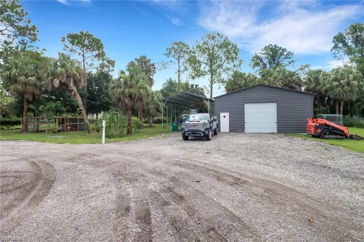 Detached garage with driveway, a detached carport, and view of scattered trees
