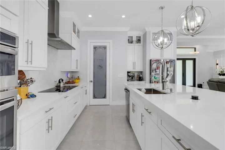 Kitchen with white cabinetry, glass insert cabinets, stainless steel appliances, crown molding, and light stone counters
