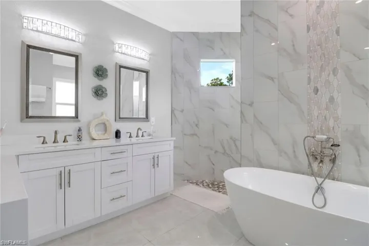 Full bath featuring a freestanding bath, double vanity, and a marble finish shower