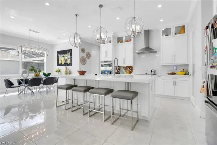 Kitchen featuring white cabinets, a breakfast bar, suspended lighting, glass insert cabinets, and stainless steel appliances