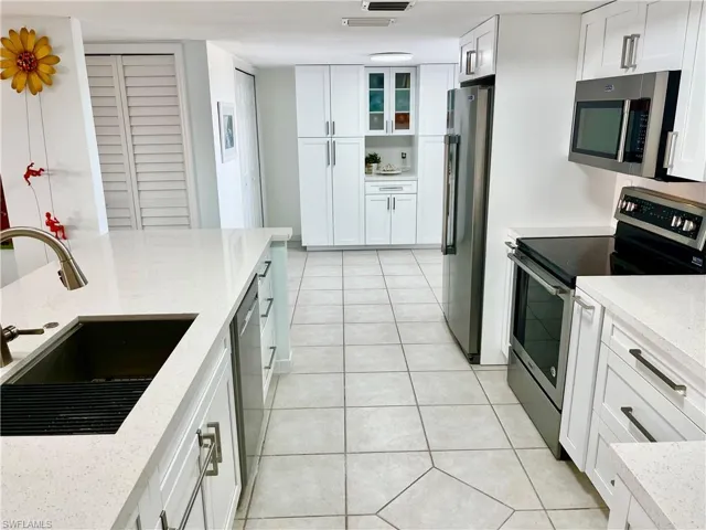 Kitchen featuring appliances with stainless steel finishes, white cabinetry, light stone counters, and sink