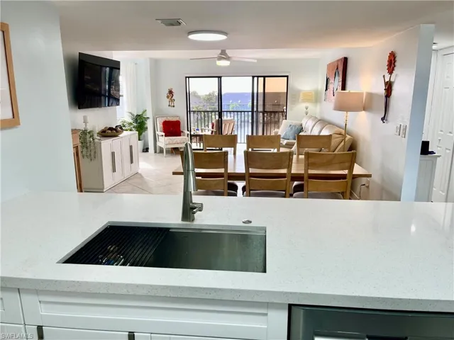 Kitchen with light tile patterned floors, light stone counters, sink, ceiling fan, and stainless steel dishwasher