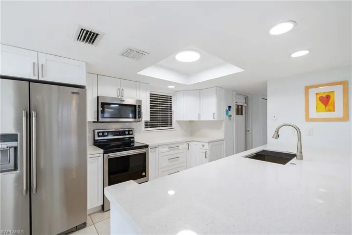 Kitchen featuring sink, white cabinetry, a tray ceiling, stainless steel appliances, and light stone countertops