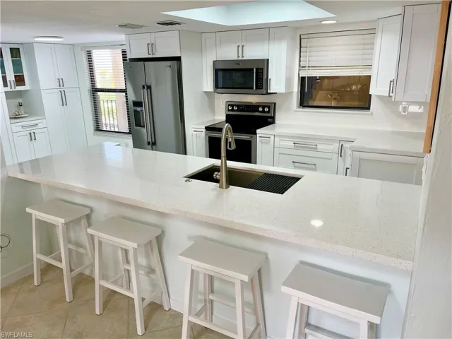 Kitchen featuring a kitchen bar, light tile patterned floors, stainless steel appliances, kitchen peninsula, and white cabinets