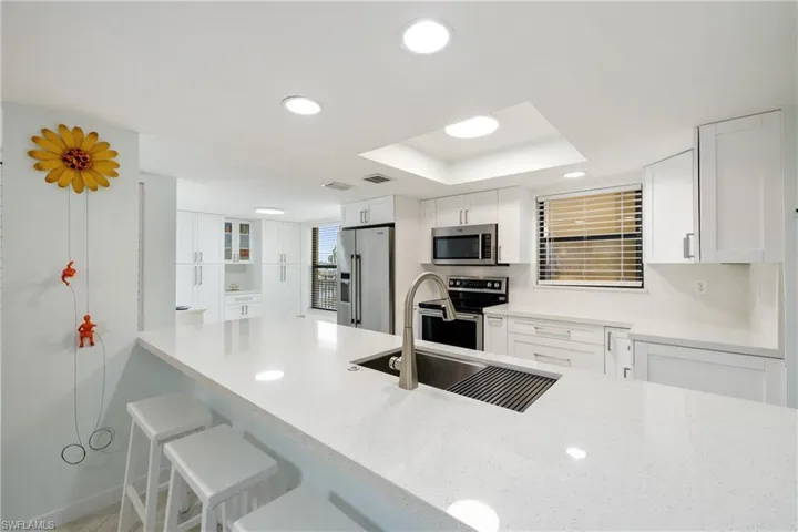 Kitchen featuring sink, white cabinets, a kitchen bar, a raised ceiling, and appliances with stainless steel finishes