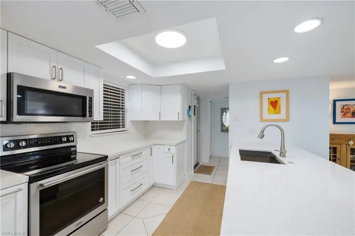 Kitchen with appliances with stainless steel finishes, a raised ceiling, white cabinetry, and sink