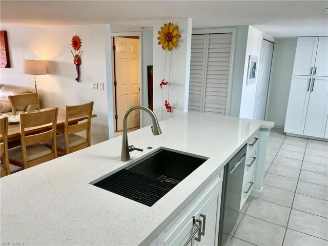 Kitchen featuring white cabinets, light stone countertops, sink, light tile patterned flooring, and stainless steel dishwasher
