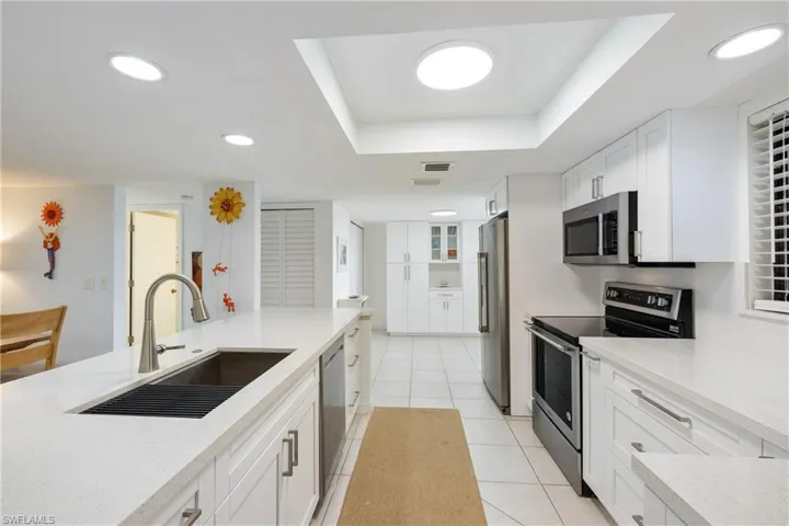 Kitchen featuring light tile patterned flooring, white cabinets, a raised ceiling, stainless steel appliances, and sink