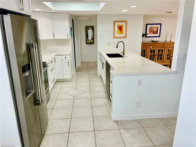 Kitchen featuring light stone countertops, high end refrigerator, white cabinetry, sink, and kitchen peninsula