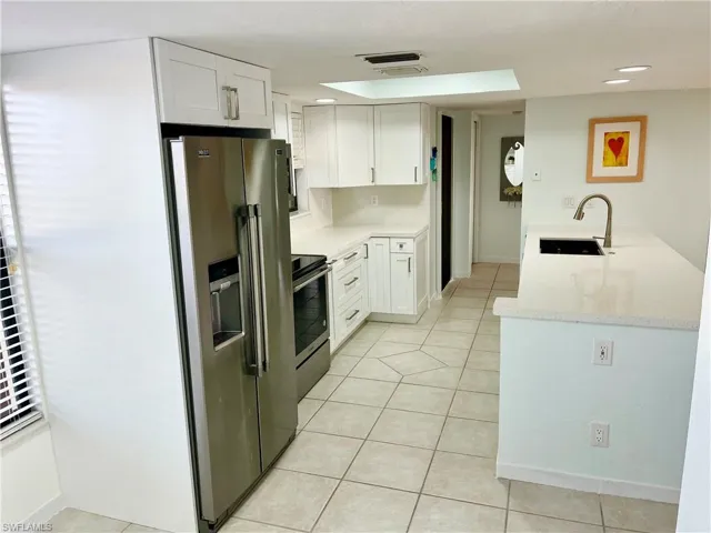 Kitchen with light tile patterned floors, stainless steel appliances, light stone counters, sink, and white cabinets