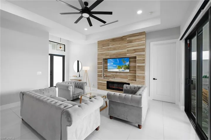Living area with a large fireplace, a tray ceiling, light tile patterned floors, a ceiling fan, and recessed lighting