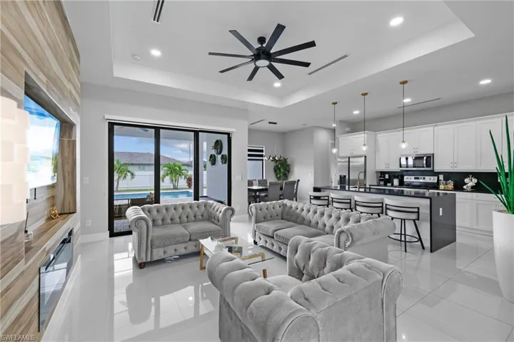 Living room with a tray ceiling, recessed lighting, light tile patterned floors, and ceiling fan