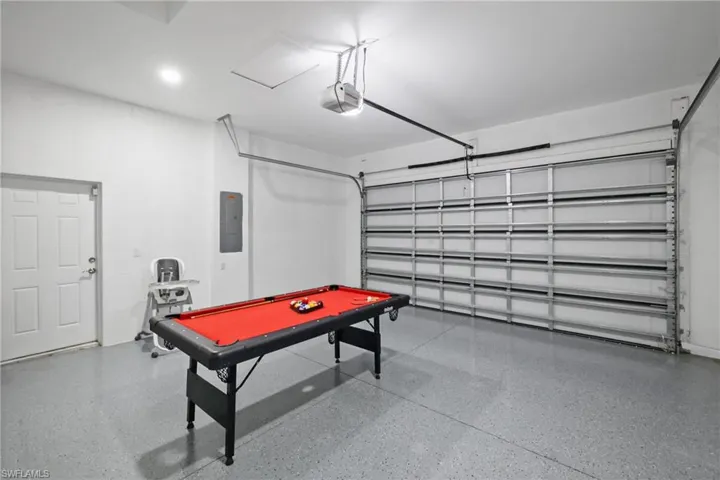 Rec room with a garage, billiards table, electric panel, and dark aggregate flooring