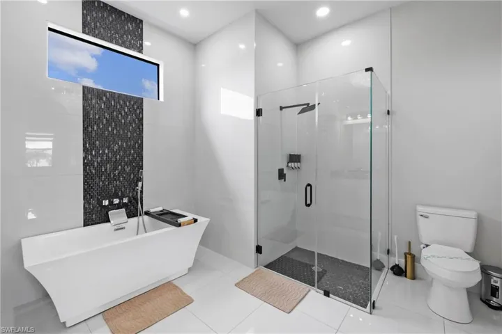 Full bathroom featuring pet washing area, a shower stall, a freestanding bath, tile patterned floors, and tile walls