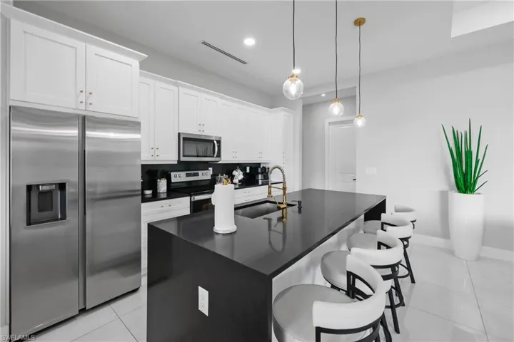 Kitchen featuring stainless steel appliances, a kitchen breakfast bar, an island with sink, light tile patterned floors, and recessed lighting