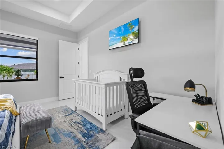 Bedroom with an office area, light tile patterned floors, and a tray ceiling