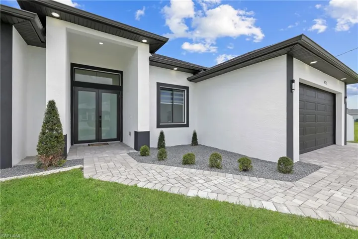 View of exterior entry with a garage, stucco siding, decorative driveway, and a yard