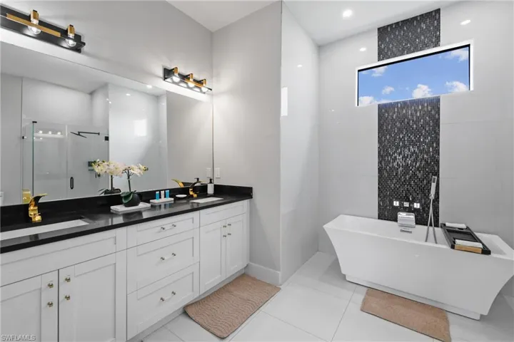 Full bathroom with double vanity, a shower stall, a freestanding tub, light tile patterned floors, and recessed lighting
