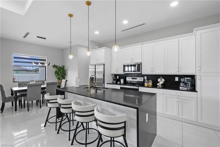 Kitchen featuring a center island with sink, stainless steel appliances, a breakfast bar, decorative light fixtures, and light tile patterned flooring