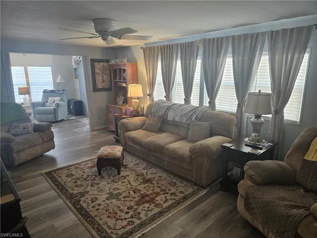 Living room with ceiling fan, dark wood-type flooring, and a wealth of natural light