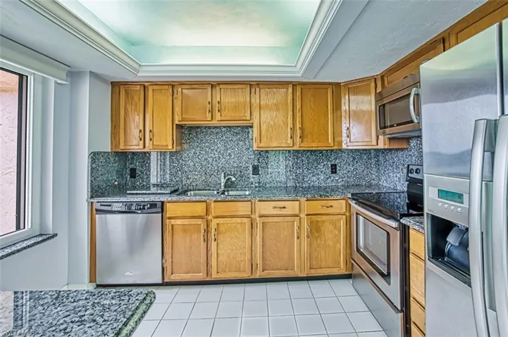 Kitchen with stainless steel appliances, backsplash, light tile patterned floors, and a tray ceiling