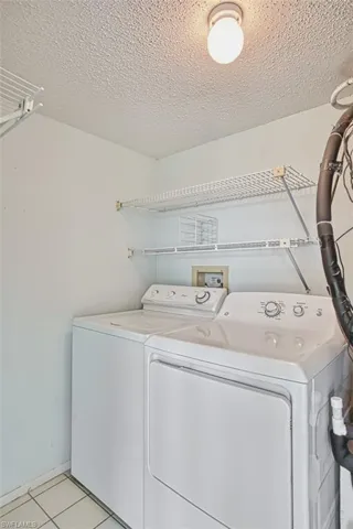 Laundry room featuring light tile patterned floors, a textured ceiling, and full size washer and dryer