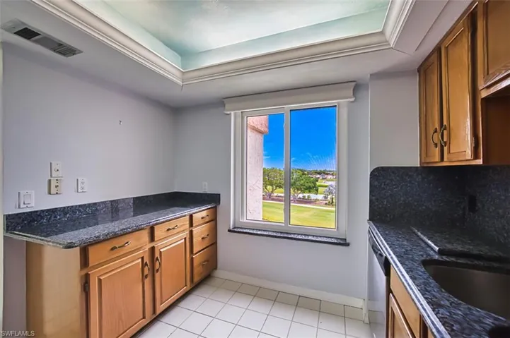 Kitchen featuring brown cabinetry, dark stone countertops, light tile patterned floors, decorative backsplash, and dishwasher