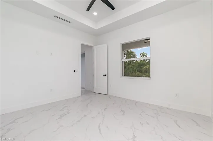 Spare room with recessed lighting, light marble finish floors, a tray ceiling, and a ceiling fan