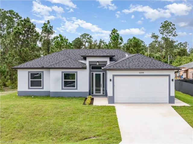 Prairie-style home with stucco siding, a shingled roof, concrete driveway, and a front lawn