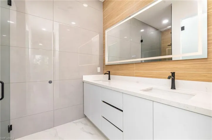Bathroom featuring tile walls, a shower stall, double vanity, light marble finish floors, and recessed lighting