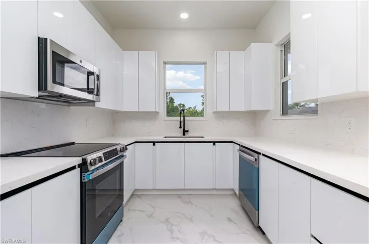 Kitchen featuring modern cabinets, appliances with stainless steel finishes, tasteful backsplash, light marble finish flooring, and white cabinetry